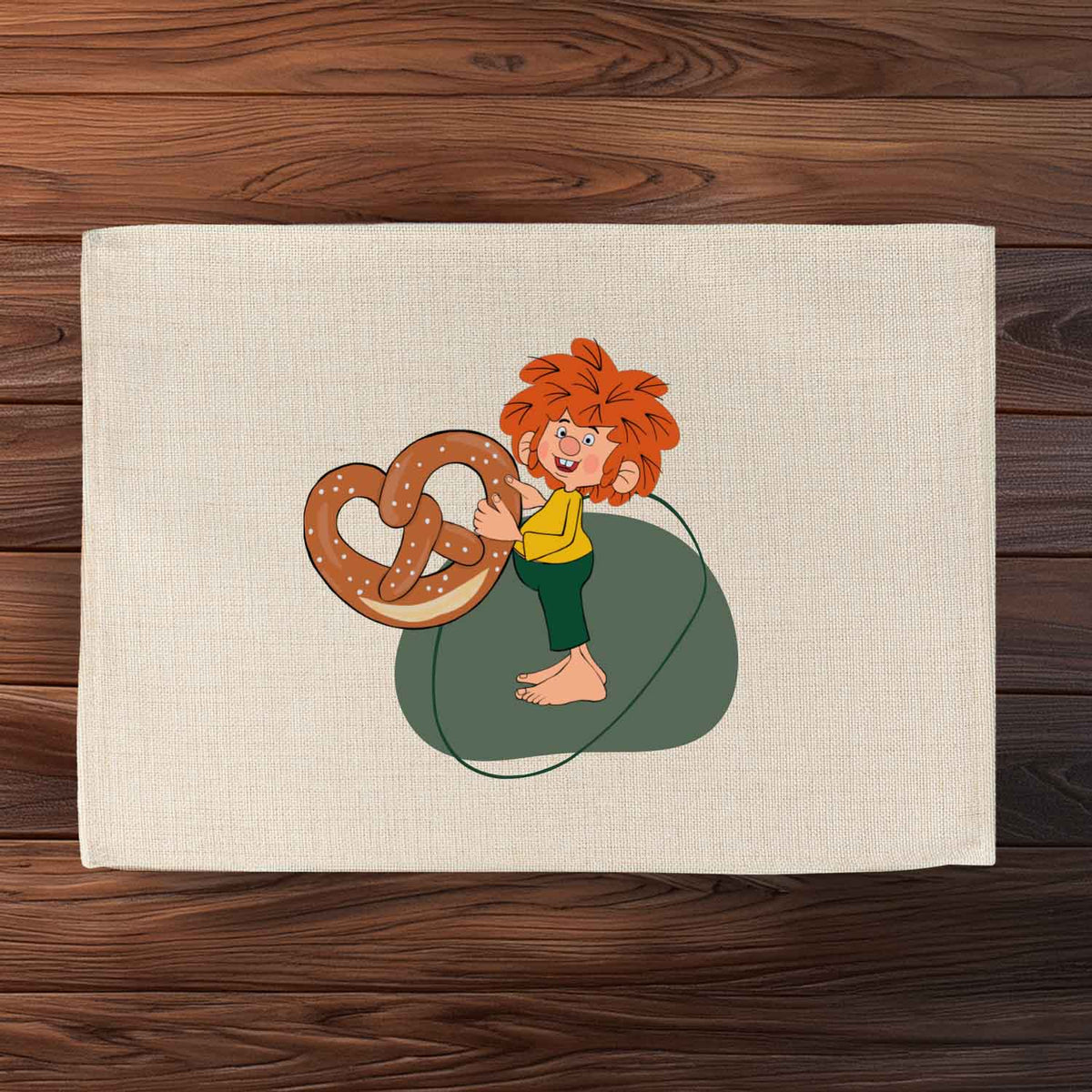 Abwaschbares Pumuckl Tischset mit Motiv des Kobolds, der eine große Brezel hält, auf hellem Stoff.