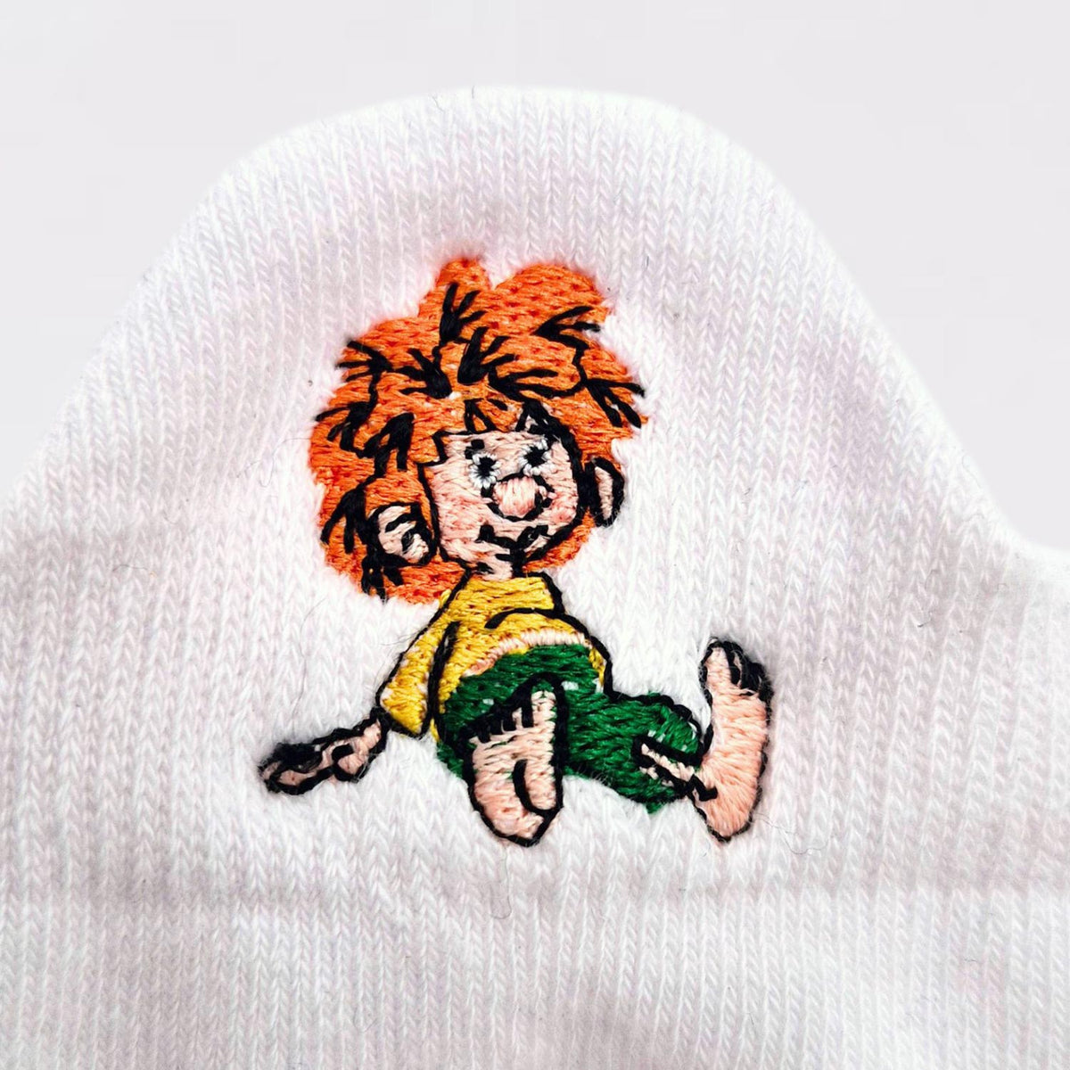 Detail der Pumuckl Stickerei auf der Sneaker Socke: Pumuckl mit roten Haaren, gelbem Hemd und grüner Hose