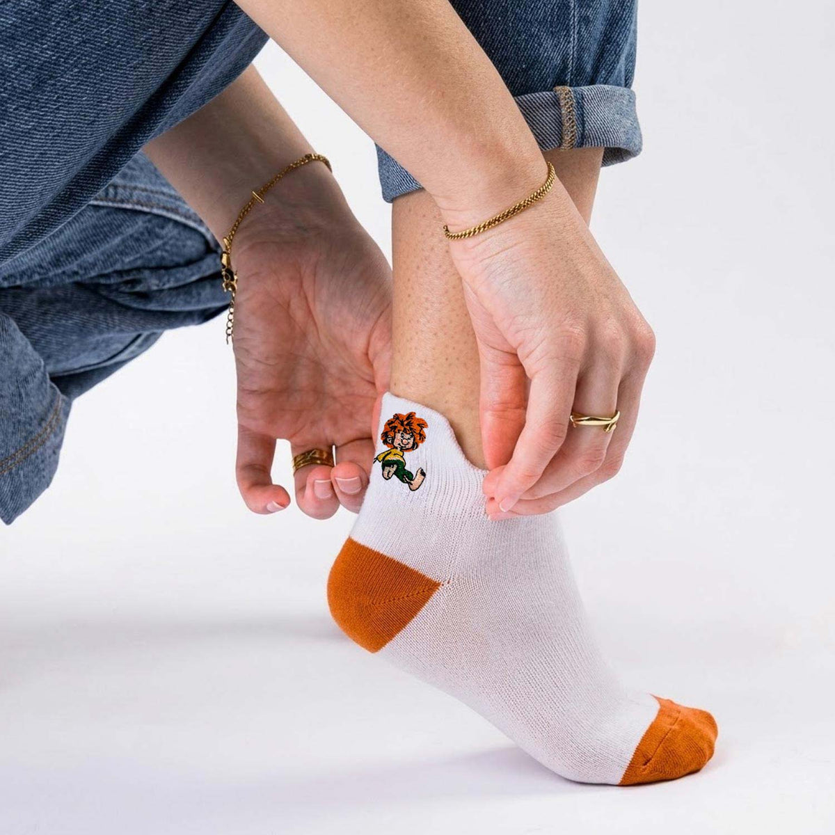 Pumuckl Sneaker Socken in Weiß mit orangefarbener Ferse und Spitze, gesticktes Pumuckl-Motiv an der Fersenlasche, getragen zu Jeans