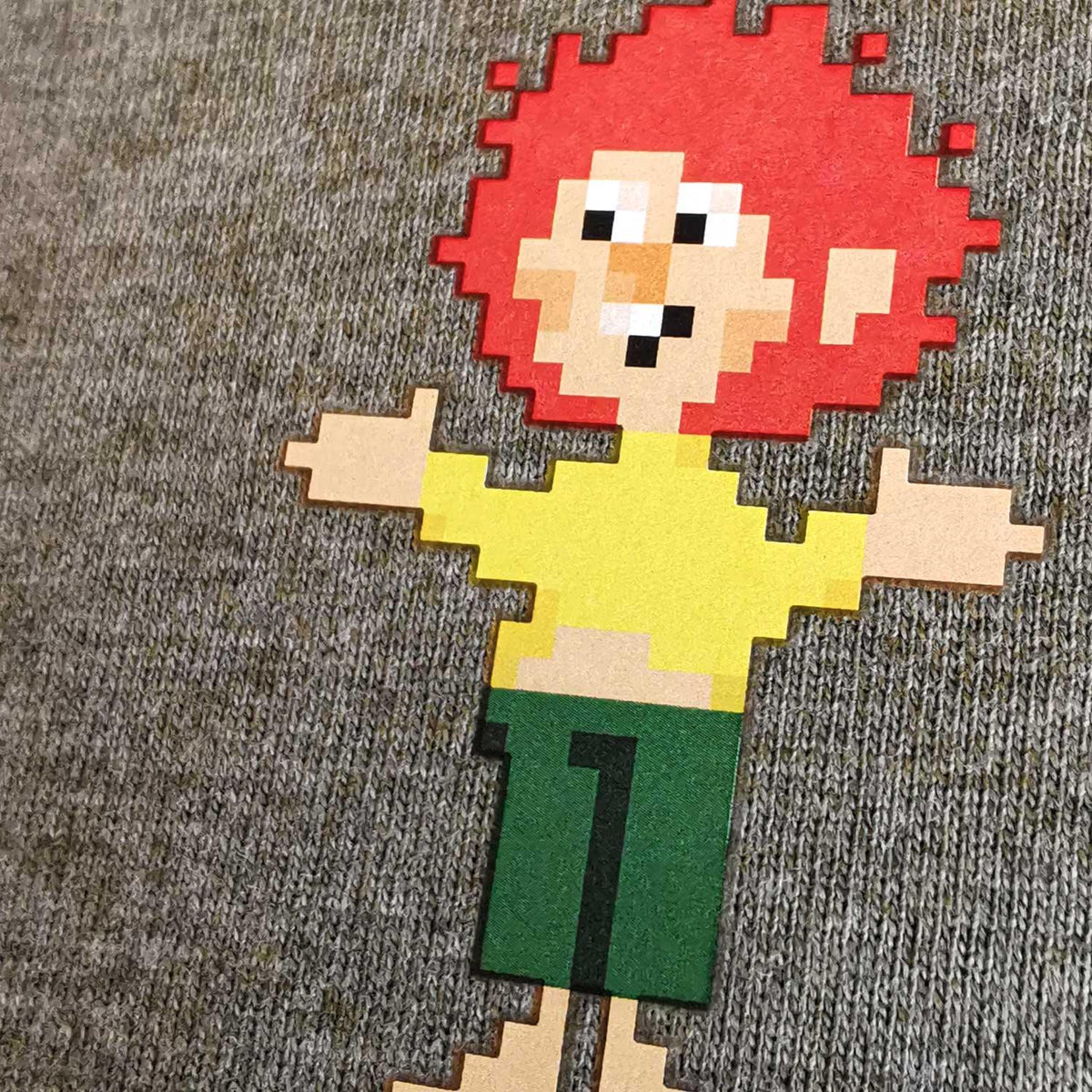 Pumuckl T-Shirt Pixmuckl Detailansicht: Pixel-Pumuckl mit roten Haaren, gelbem Oberteil auf grauem Stoff