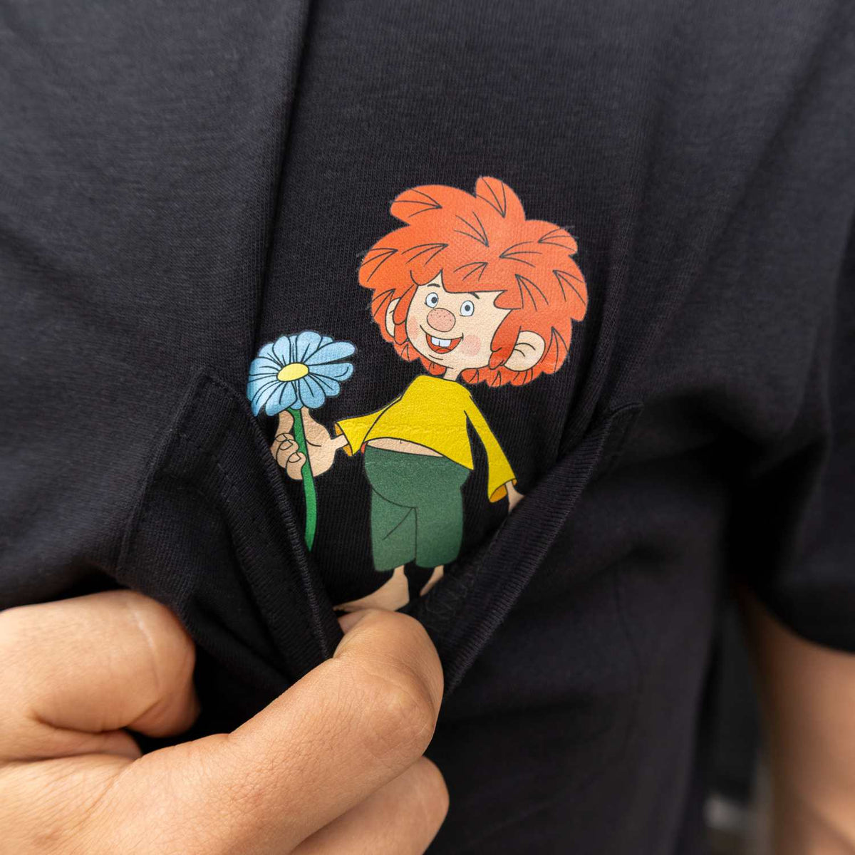 Nahaufnahme Pumuckl T-Shirt Schabernack: Der Kobold schaut aus der Brusttasche und hält eine blaue Blume hoch