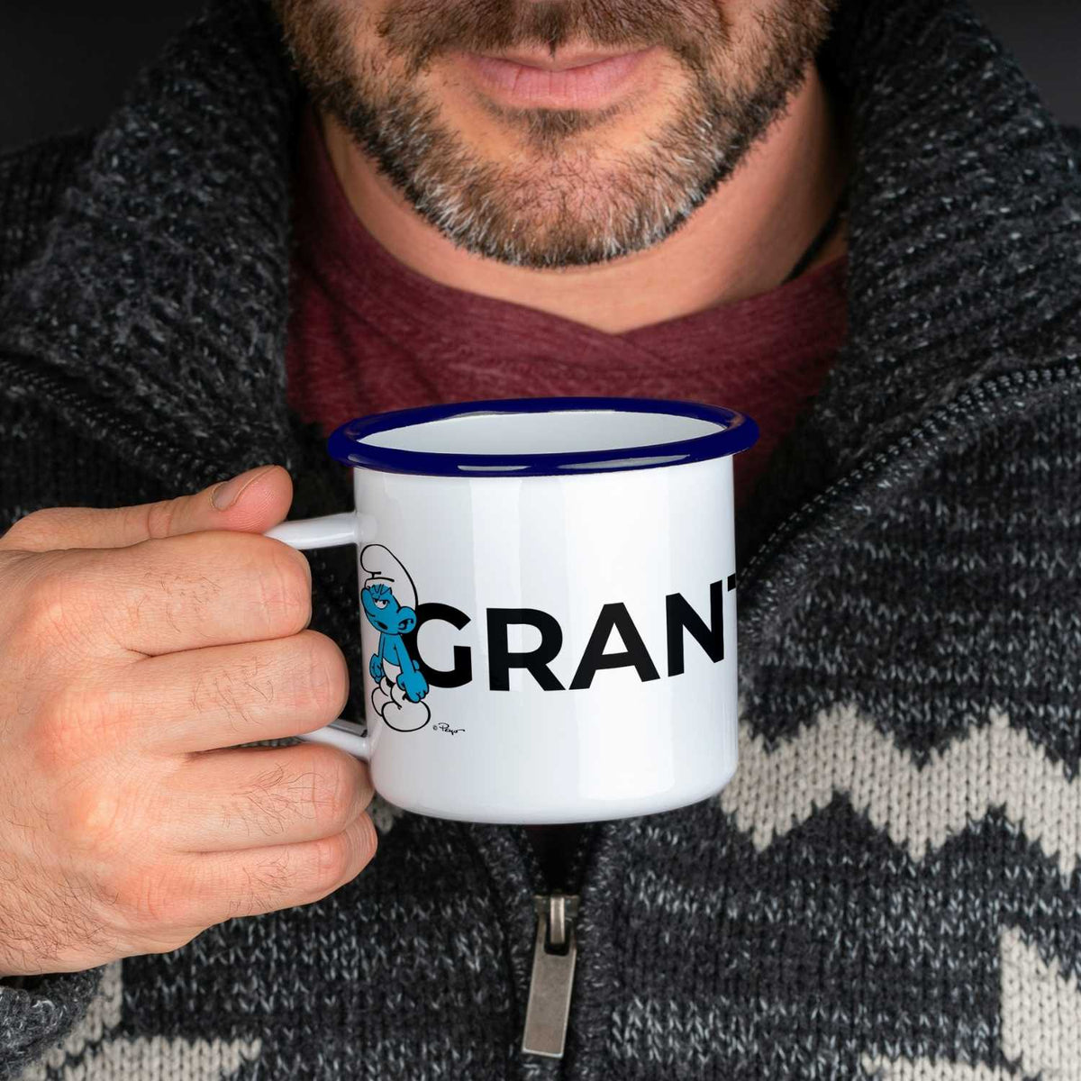 Man hält ®Die Schlümpfe Emailletasse Grantla mit blauem Rand und Schlumpf-Motiv in der Hand