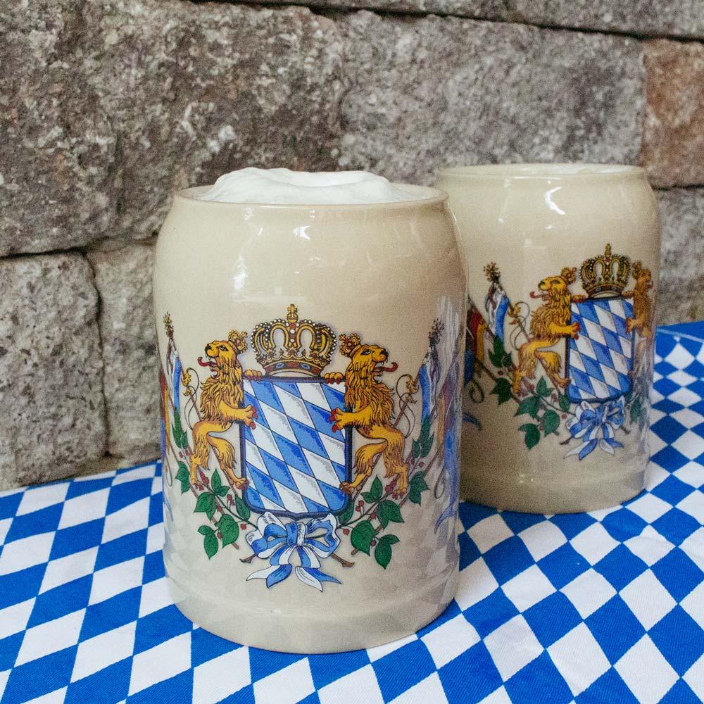 Zwei bayerische Steinkrüge mit Wappen vor einer Natursteinmauer auf weiß-blauer Rautentischdecke